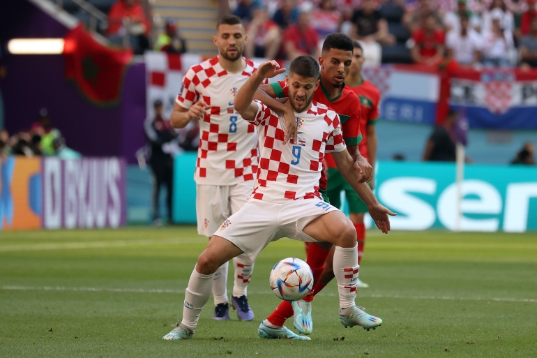 Morocco player has arm around Croatian player's neck, as the latter wrestles with the ball