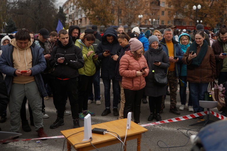 People in winter clothes gathered around a satellite link to get mobile phone coverage and speak to their families.
