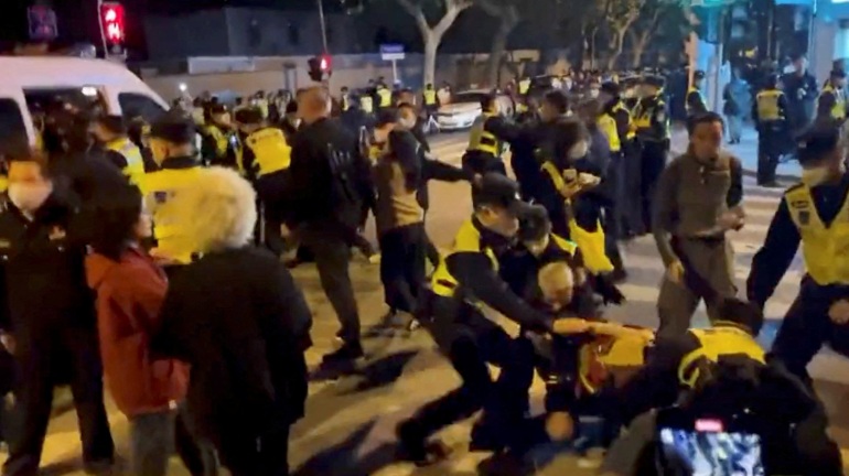 Police officers in high visibility jackets detaining people at a protest in Shanghai, China.