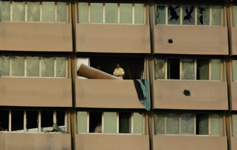 A photo of the side of a building with windows and a hole in one of the balconies.