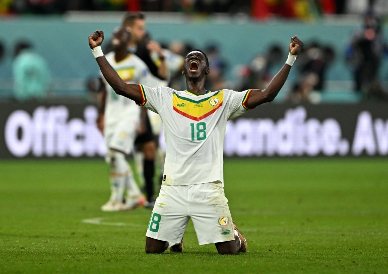Senegal's Ismaila Sarr celebrates qualifying for the knockout stages by crying out while on his knees with arms raised in victory.