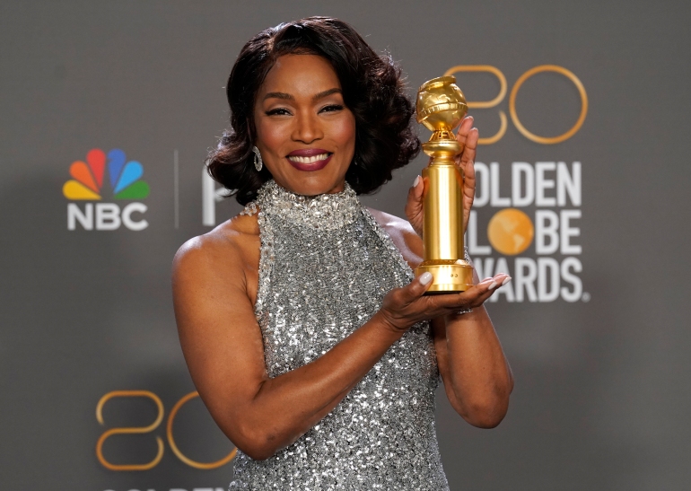 Angela Bassett in a sliver sleeveless high necked evening gown holding her Golden Globe with both hands and smiling.