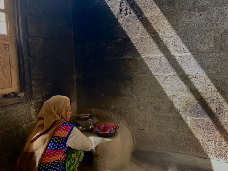 A photo of a woman crouching on a little rock-like table attached to a brick wall with two bowls on it. The woman is having at the brick wall that the table is attached to.