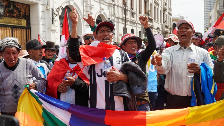 Protesters behind a colorful banner chant and raise their fists in the streets of Lima, Peru.
