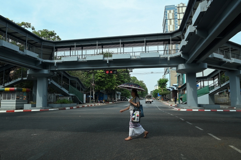 A woman crosses a near-empty street in Yangon. She is carrying an umbrella to protect herself from the sun